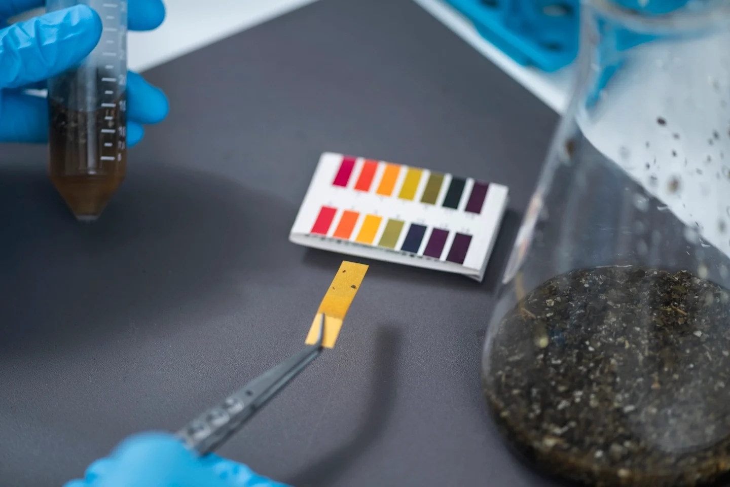 Gloved hands in an agricultural lab testing the pH of water from inside of a beaker.
