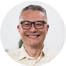 Headshot of a man with salt and pepper hair, black glasses, and a tan button-up shirt.