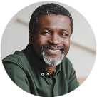 Headshot of a Black man with grey in his beard and a green button-up shirt.